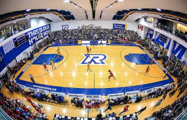 A yellow and blue basketball court with a game going on infront of a surrounding crowd.