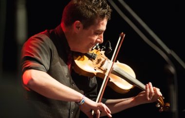 Homme avec chemise noire jouant du violon.