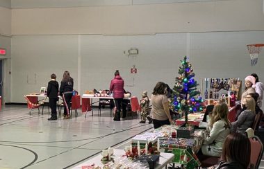 Plusieurs tables dans un gymnase accompagné des créateurs avec des décorations de Noël et des visiteurs qui observent les articles à vendre.