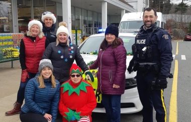 Volunteers collecting food bank donations pose for a photo in front of an RCMP cruiser