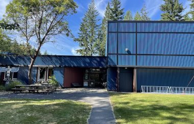 A paved path leads to a blue-roofed building, with trees and sunshine.