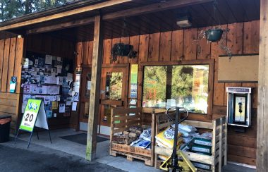 A storefront on Cortes Island has wooden siding and displays a lottery ticket sign, notice board and pay phone.