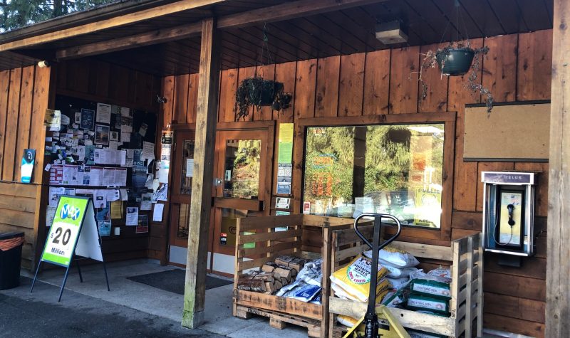 A storefront on Cortes Island has wooden siding and displays a lottery ticket sign, notice board and pay phone.