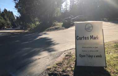 A sign indicates the driveway leading to a parking lot outside the Cortes Market general store.