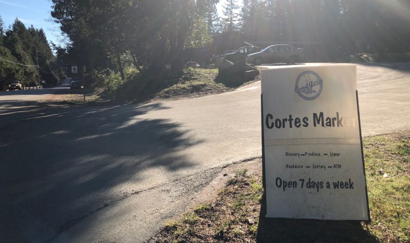 A sign indicates the driveway leading to a parking lot outside the Cortes Market general store.
