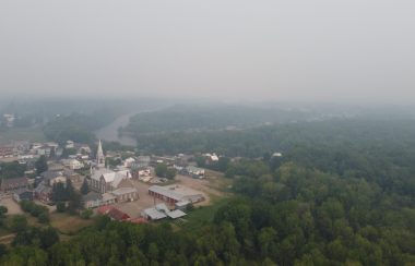A drone photo of a small town surrounded by forest with a thick layer of smoke from forest fires.