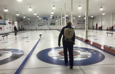 A man standing on a sheet of curling ice spraying it with water