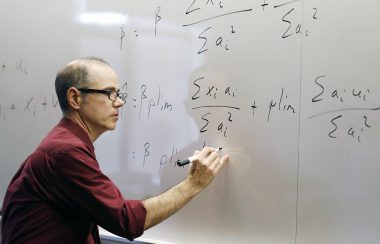A man writes economics equations on a white board