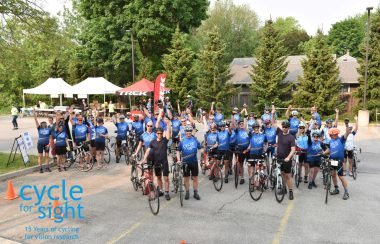 On peut voir des dizaines de cyclistes posant avec leur vélo dans un stationnement et portant le dossard bleu de l'événement « Cycle for Sight ».