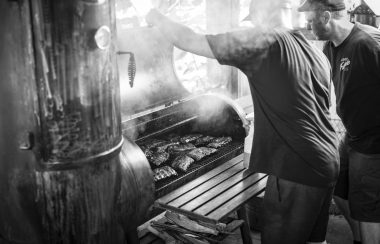 A black and white professional photo of two men opening a barbeque.