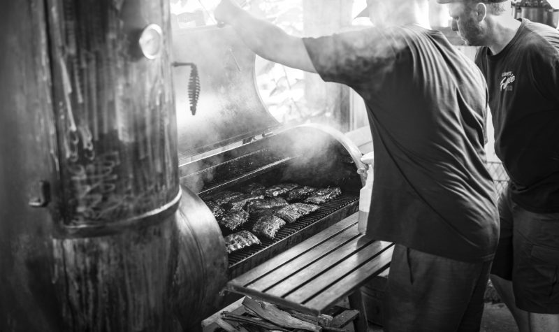 A black and white professional photo of two men opening a barbeque.