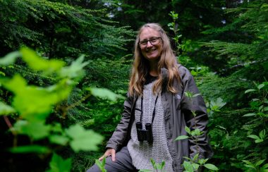 A woman stands in the middle of a forest.