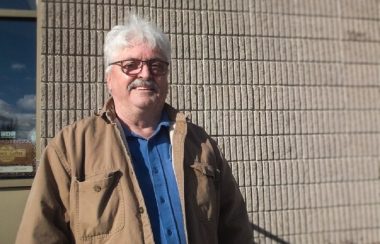 Un homme eu cheveux gris devant un mur de brique