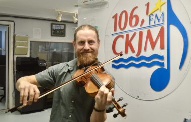 Un homme jouant du violon en avant du logo de Radio CKJM.