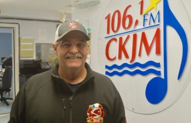 Un homme portant une casquette et un gilet noir en avant du logo de Radio CKJM.