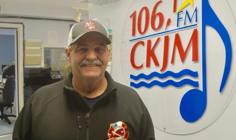 Un homme portant une casquette et un gilet noir en avant du logo de Radio CKJM.
