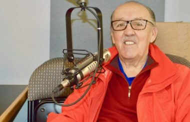 Un homme portant un gilet rouge au micro dans un studio de radio.