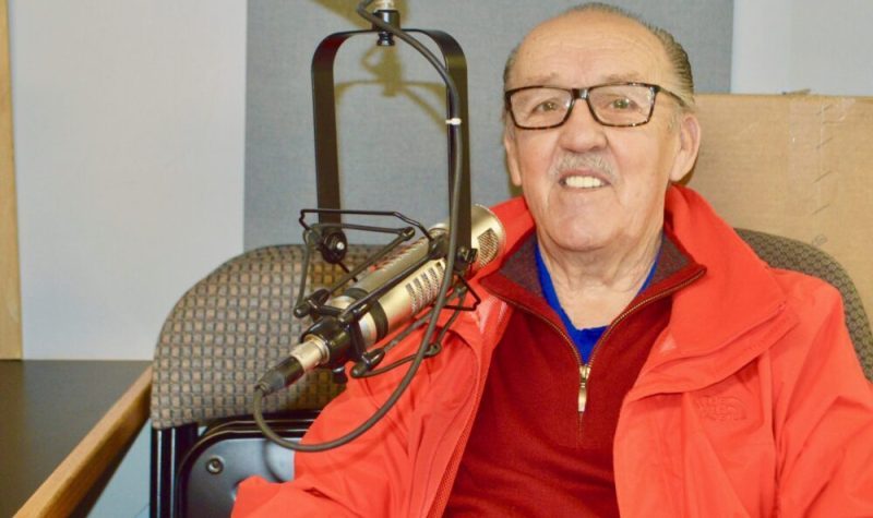 Un homme portant un gilet rouge au micro dans un studio de radio.