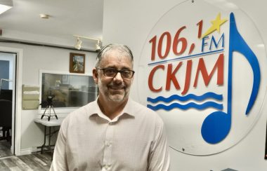 Un homme debout en avant du logo de Radio CKJM.