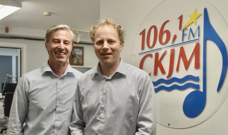 Deux hommes portant des chemises bleu en avant du logo de Radio CKJM.