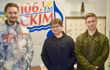 Un homme et deux jeunes garçons en avant du logo de Radio CKJM.