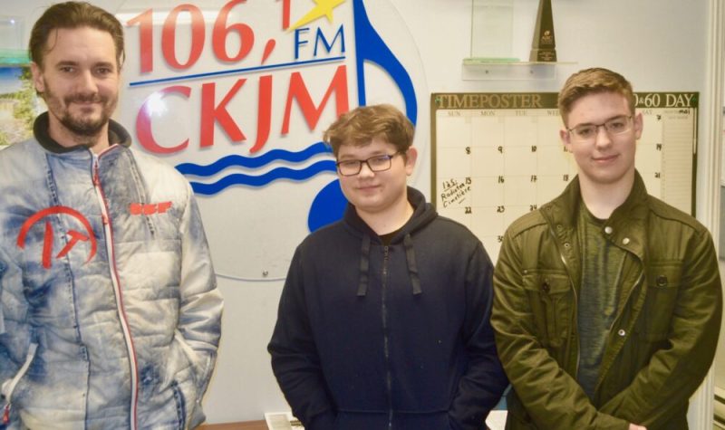 Un homme et deux jeunes garçons en avant du logo de Radio CKJM.
