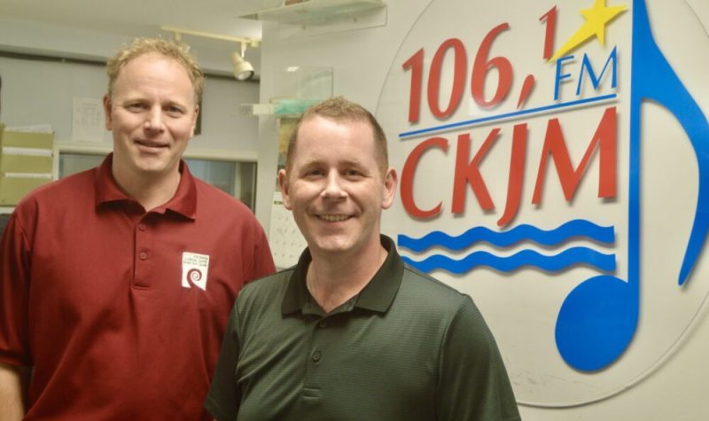 Un homme portant un chandail rouge et un homme portant un chandail vert en avant du logo de Radio CKJM.