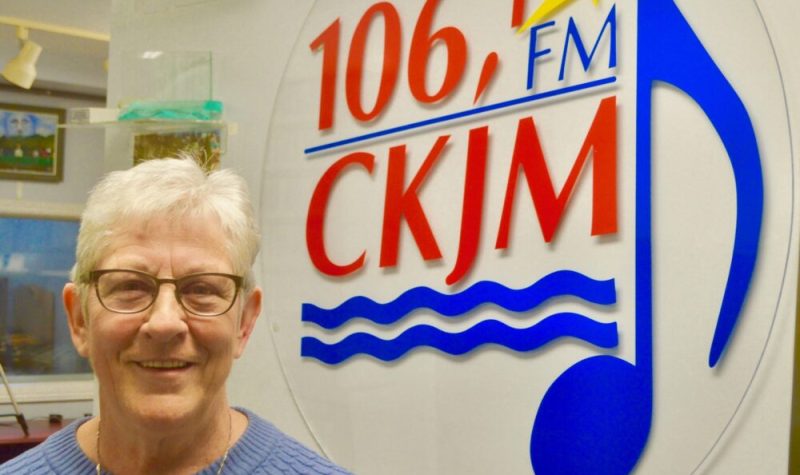 Une femme avec un chandail bleu en avant du logo de Radio CKJM.