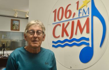 Un homme poratnt un chandail bleu en avant du logo de Radio CKJM.