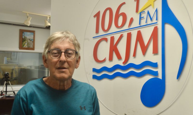 Un homme poratnt un chandail bleu en avant du logo de Radio CKJM.