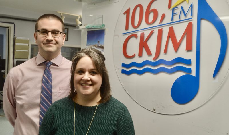 Un homme et une femme en avant du logo de Radio CKJM