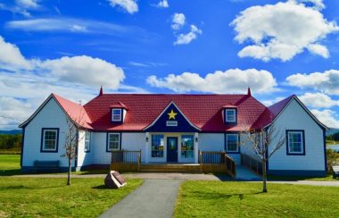 Édifice en bois aux couleurs de l'Acadie et avec trois pignons par une journée ensoleillée d'été.