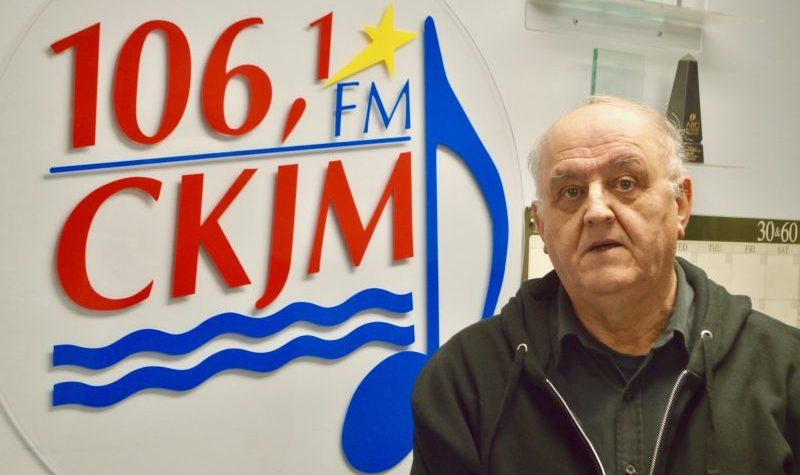Un homme assez âgé en avant du logo de Radio CKJM.