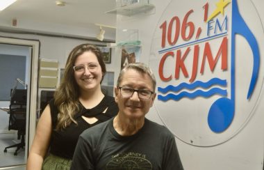 Un homme et une femme habillés en noir en avant du logo de Radio CKJM.