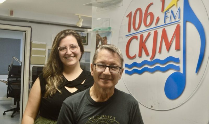 Un homme et une femme habillés en noir en avant du logo de Radio CKJM.