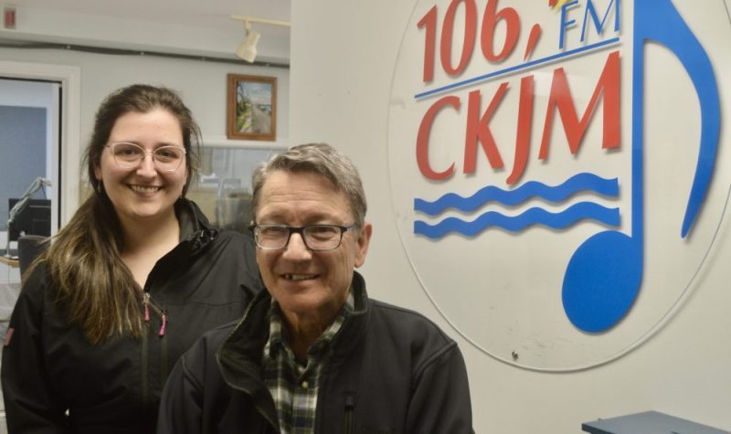 Un homme et une femme en avant du logo de Radio CKJM.
