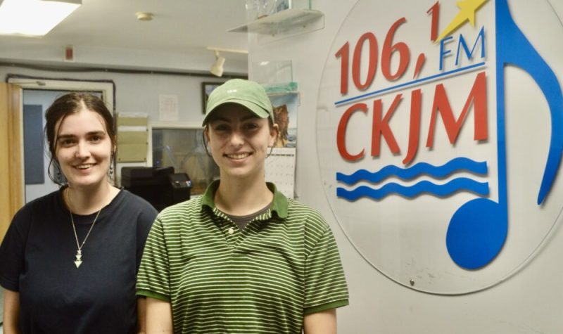 Deux jeunes filles en avant du logo de Radio CKJM.