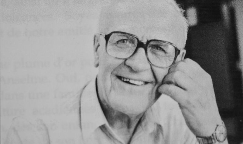 Homme âgé avec lunettes et chemise blanche souriant à la caméra.