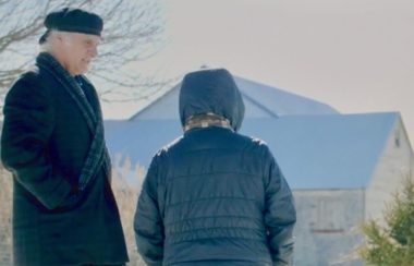 Un homme avec un chapeau et un manteau noir parlant à une femme portant un gilet bleu.