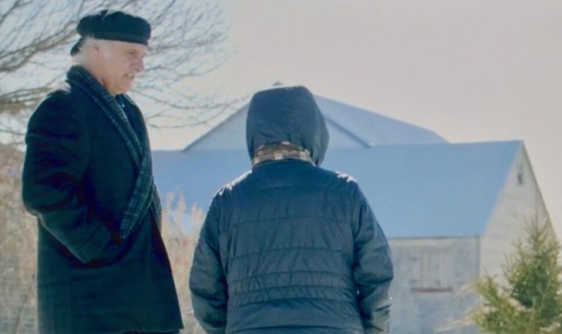 Un homme avec un chapeau et un manteau noir parlant à une femme portant un gilet bleu.