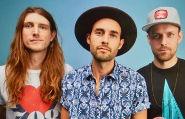 Trois hommes musiciens en avant d'un mur de couleur bleu.