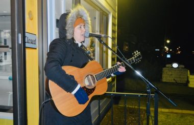 Une jeune dame avec une guitare chantant dans un micro à l'extérieur.