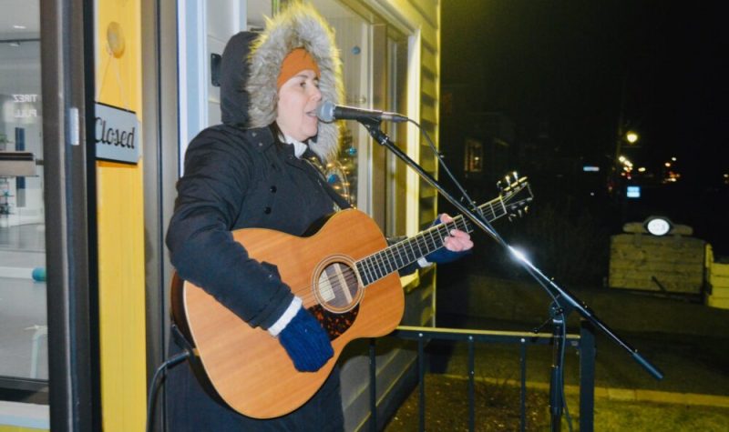 Une jeune dame avec une guitare chantant dans un micro à l'extérieur.