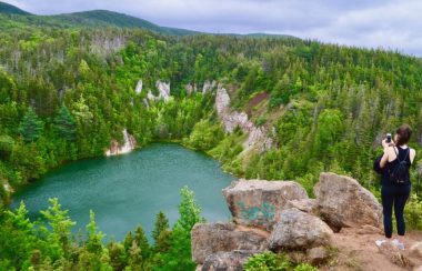 Une dame habillée en noir debout sur un rocher admirant un lac entouré de montagnes de plâtre.