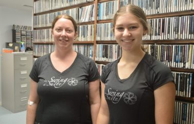 Deux dames portant des chandails noirs en avant d'une bibliothèque de disques compacts.