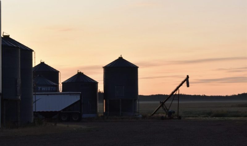 Un levé de soleil derrière quarte silos à grains et un camion semi-remorque.