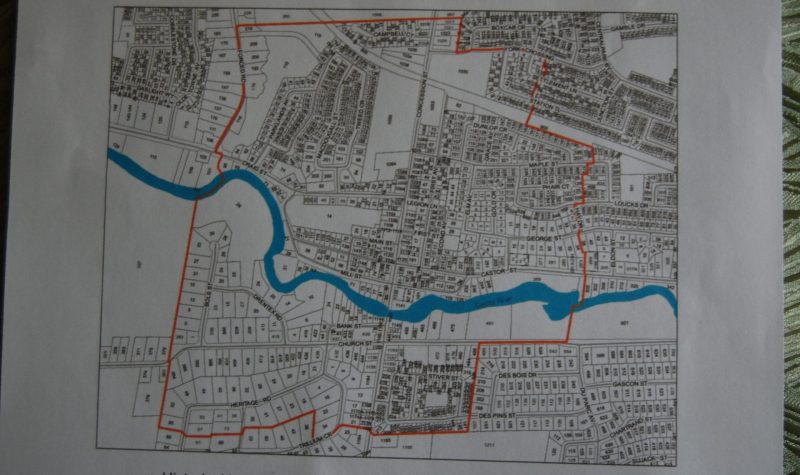 A black and white map shows a small village with a small blue river running through it and a red outline in a smaller portion of the village. The red outline marks the boundary of the actual Police Village of Russell.