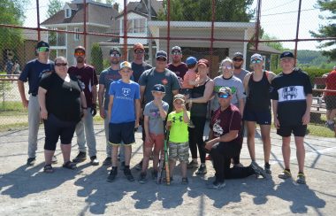 A group of people pose for a photo in front of the backstop after a baseball tournament.