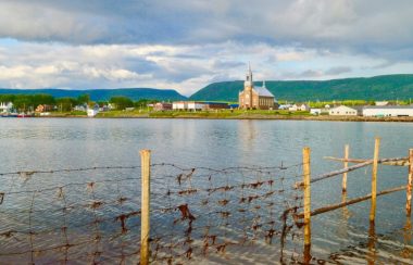 Village avec église et bâtiments situé au pieds des montagnes avec une baie en avant plan.