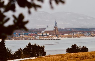 Église, école et maison au pieds des montagnes avec une baie en avant plan.